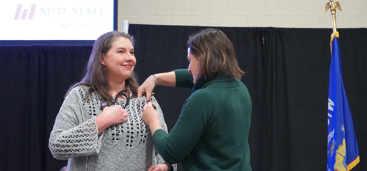 A Nursing graduate receives her pin from her chosen representative as they both stand on stage.