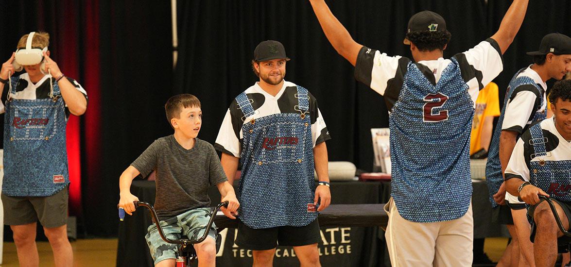 A Rafters Meet and Greet participant competes in tricycle racing against a Rafters player at the “Rafters Meet-and-Greet” and “Cuts 4 Kids” event held on Mid-State’s Wisconsin Rapids Campus, June 11.