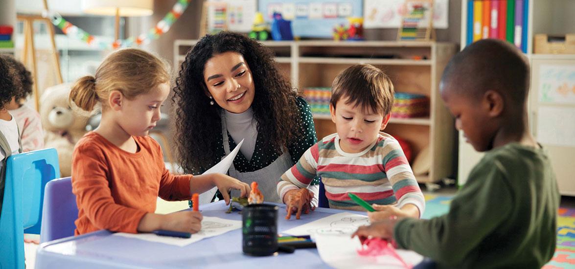 Teacher working with several small children at a table in a classroom.