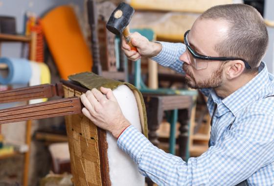 A man wearing safety glasses hammers fabric onto a chair.