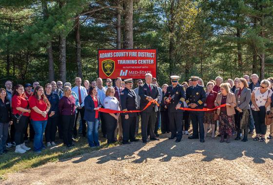 Mid-State Technical College staff and Adams County Fire District leadership look on while Rick Anderson, dean of Mid-State’s Adams Campus and School of Public Safety, helps Fire Chief Rodger Lauritzen of the Adams County Fire District cut the ribbon on the site of the Adams County Fire District Training Center in Adams, Oct. 8, 2025.