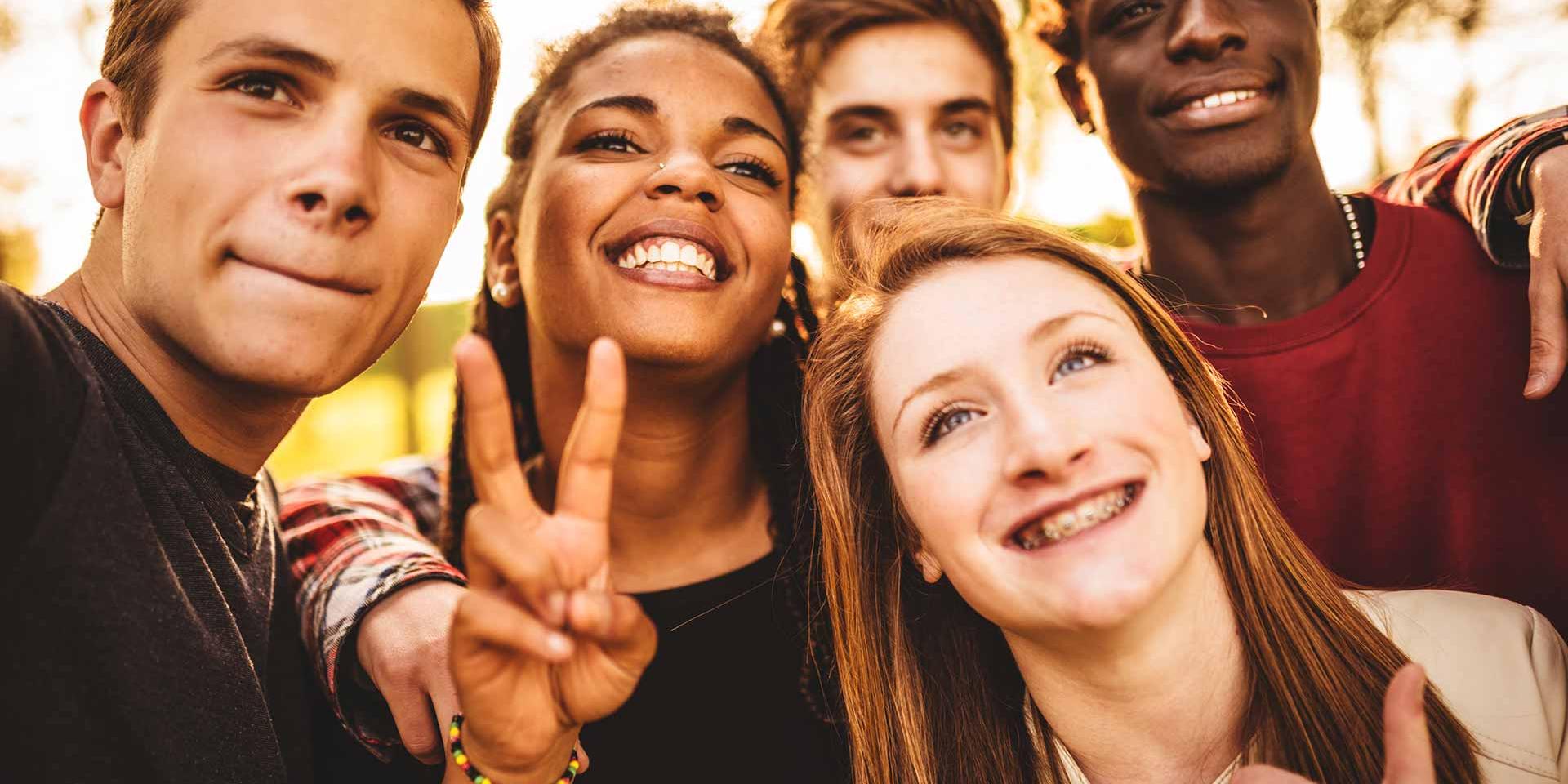 A group of five diverse students taking a fun selfie outside.